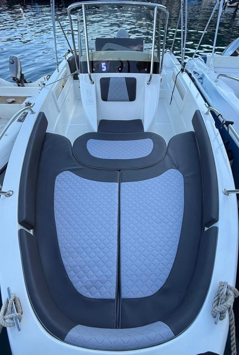 Abitacolo di una barca con cuscini e tendalino blu navy, affacciato su un porticciolo e acque calme al crepuscolo.