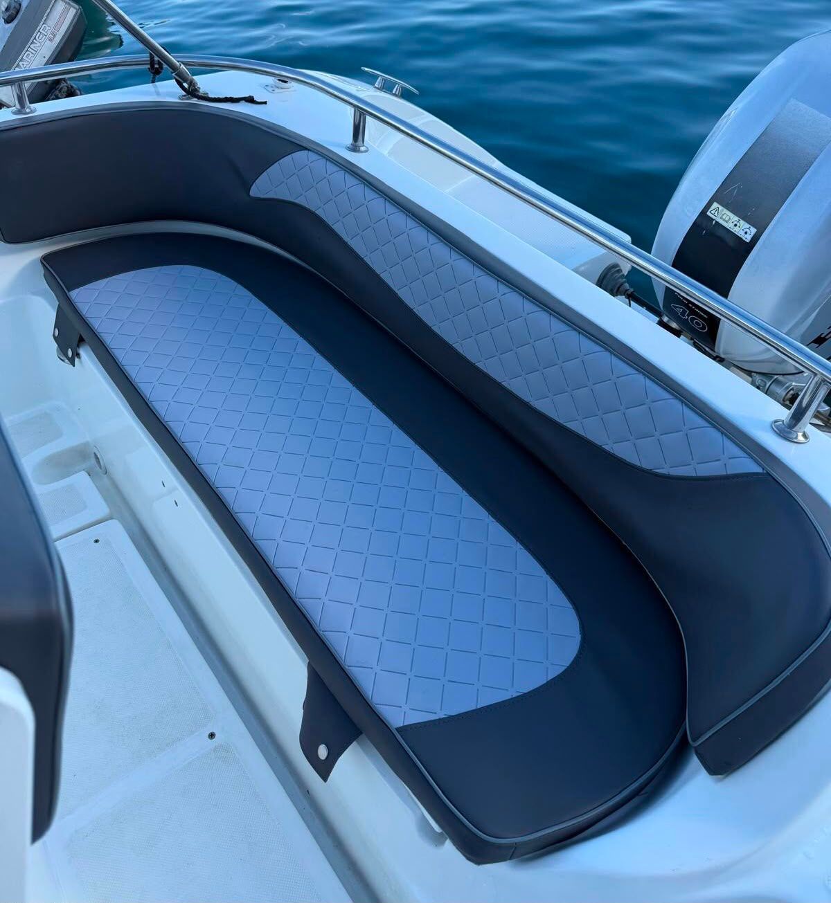 Abitacolo di una barca con cuscini e tendalino blu navy, affacciato su un porticciolo e acque calme al crepuscolo.