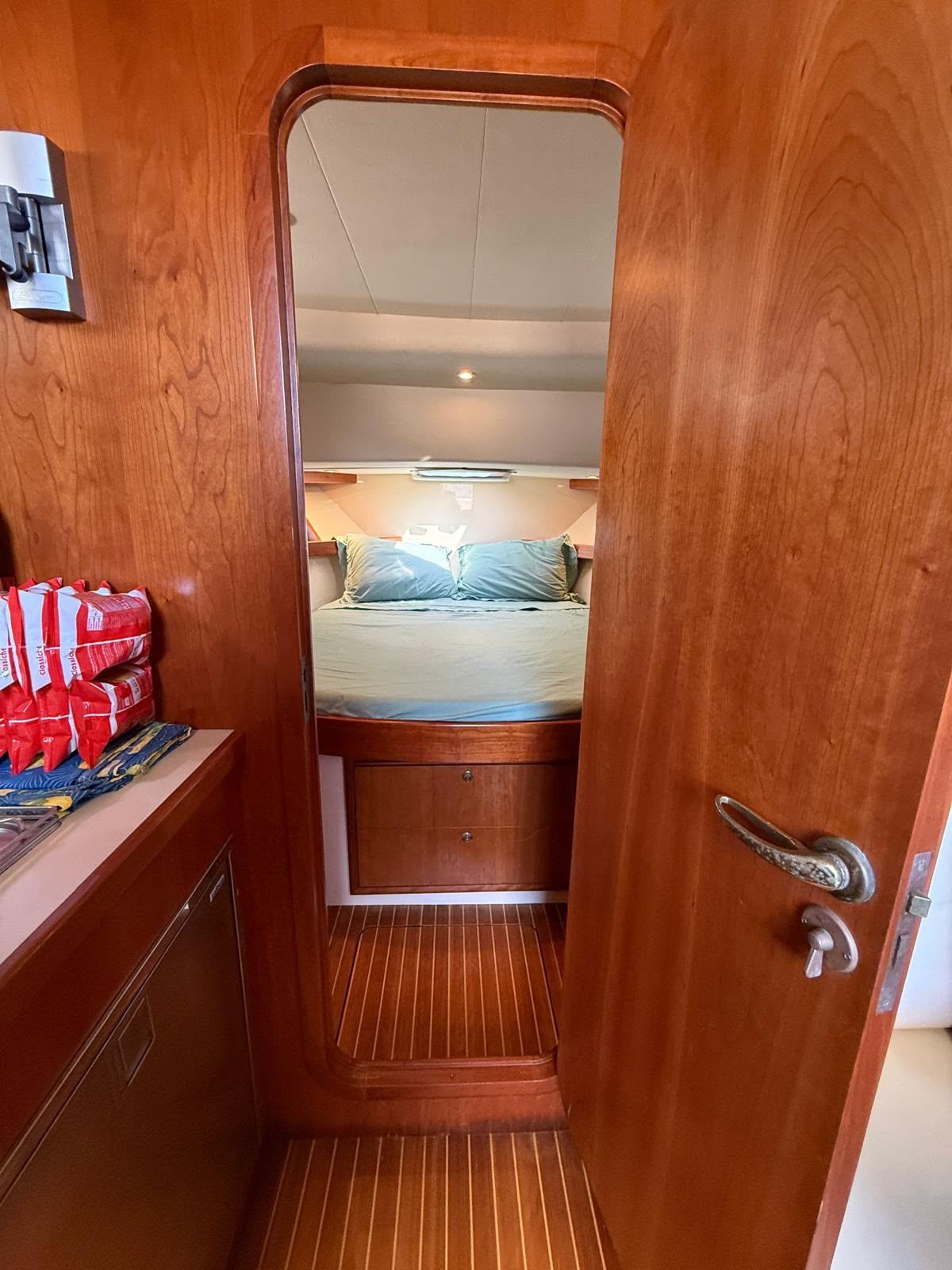 Yacht a motore bianco e blu su acque calme, con un villaggio costiero collinare e un edificio bianco con cupola sullo sfondo.