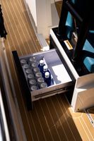 Cassetto aperto con bottiglie d'acqua e tazze accanto a un corridoio con moquette e panca nera.