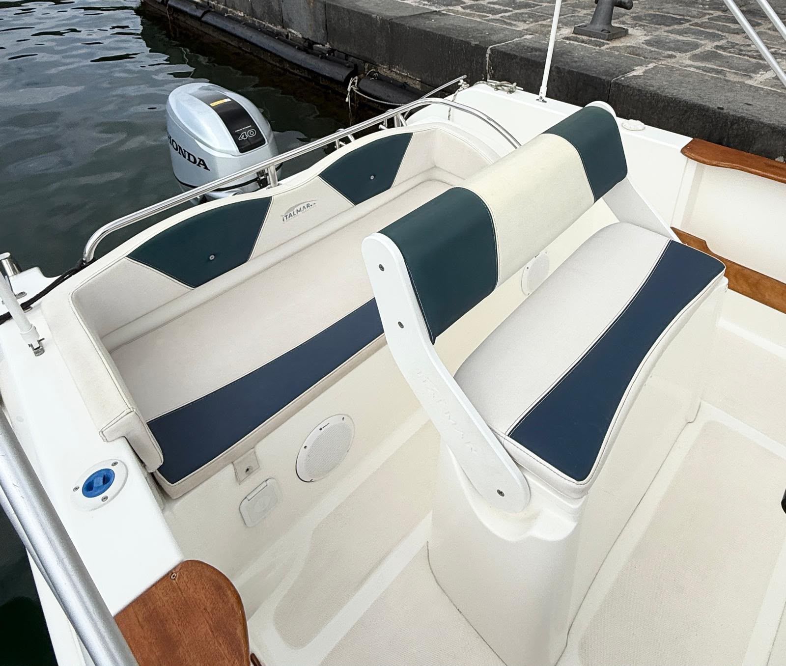 Postazione di comando dell'imbarcazione con volante bianco, pannello strumenti nero e ringhiere in acciaio inox affacciate sull'acqua.