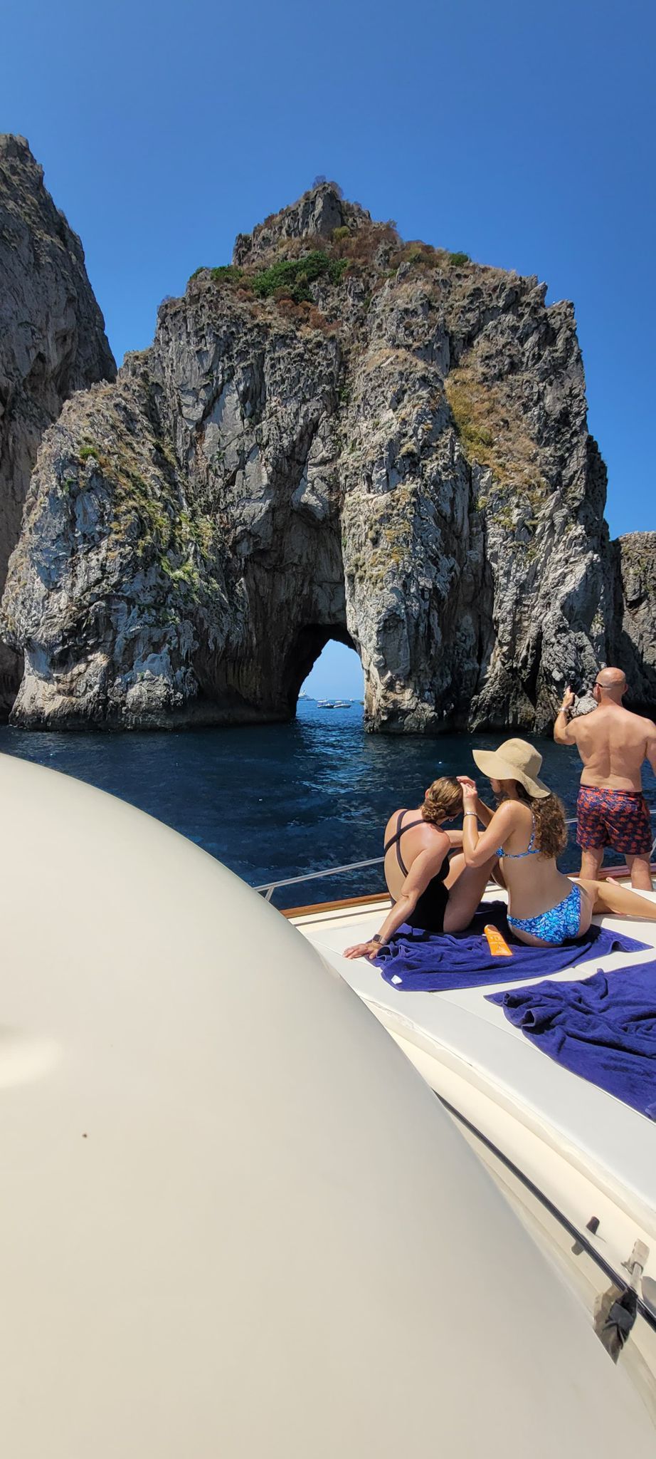 I turisti prendono il sole su una barca vicino a un grande arco roccioso in mezzo al mare, sotto un cielo azzurro e limpido.