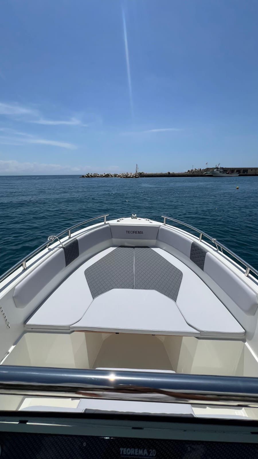 Vista dalla prua di una barca su acque azzurre verso una costa lontana, sotto un cielo limpido.