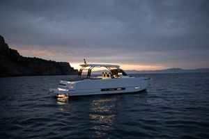 Yacht bianco su acque calme al crepuscolo, con la costa scura e il cielo nuvoloso sullo sfondo.