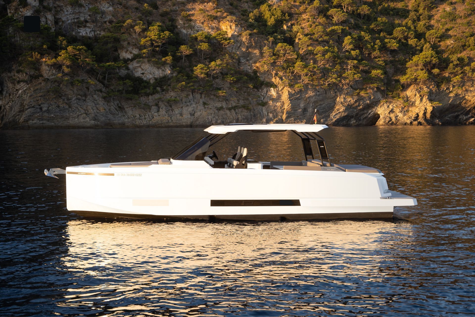 Yacht a motore bianco che naviga su acque calme accanto a una costa rocciosa e alberata.