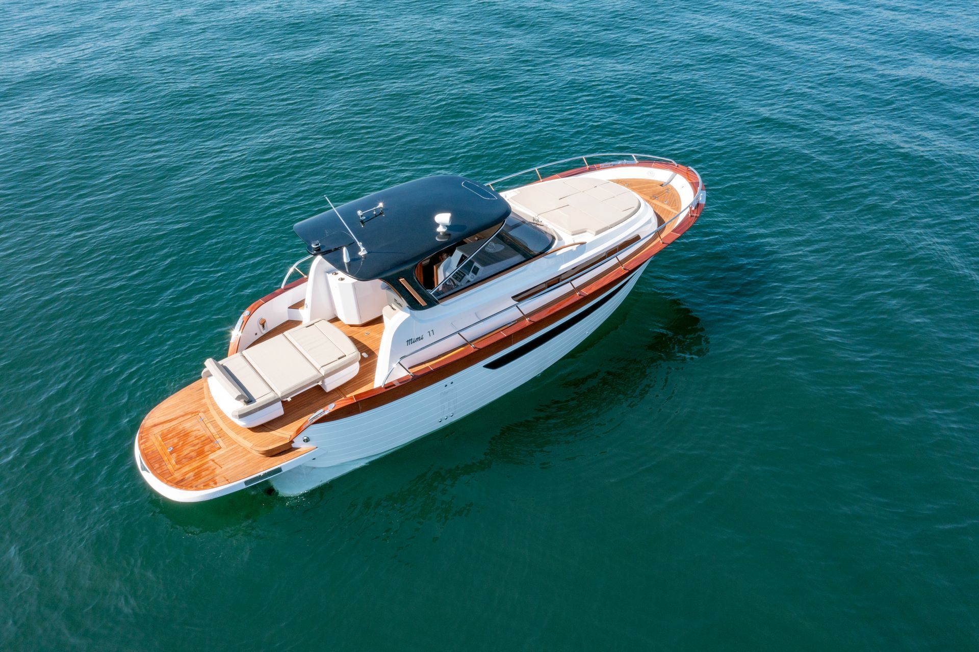 Yacht bianco con ponte in legno che naviga su acque cristalline, visto dall'alto.
