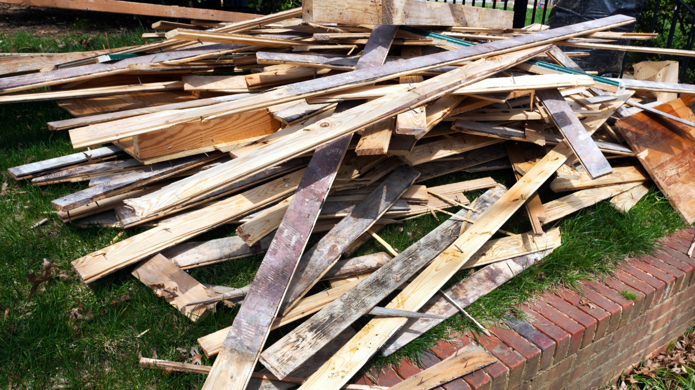 Pile of weathered wooden planks on grass next to a brick border.