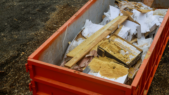 Orange dumpster filled with construction debris, including wood and cardboard.