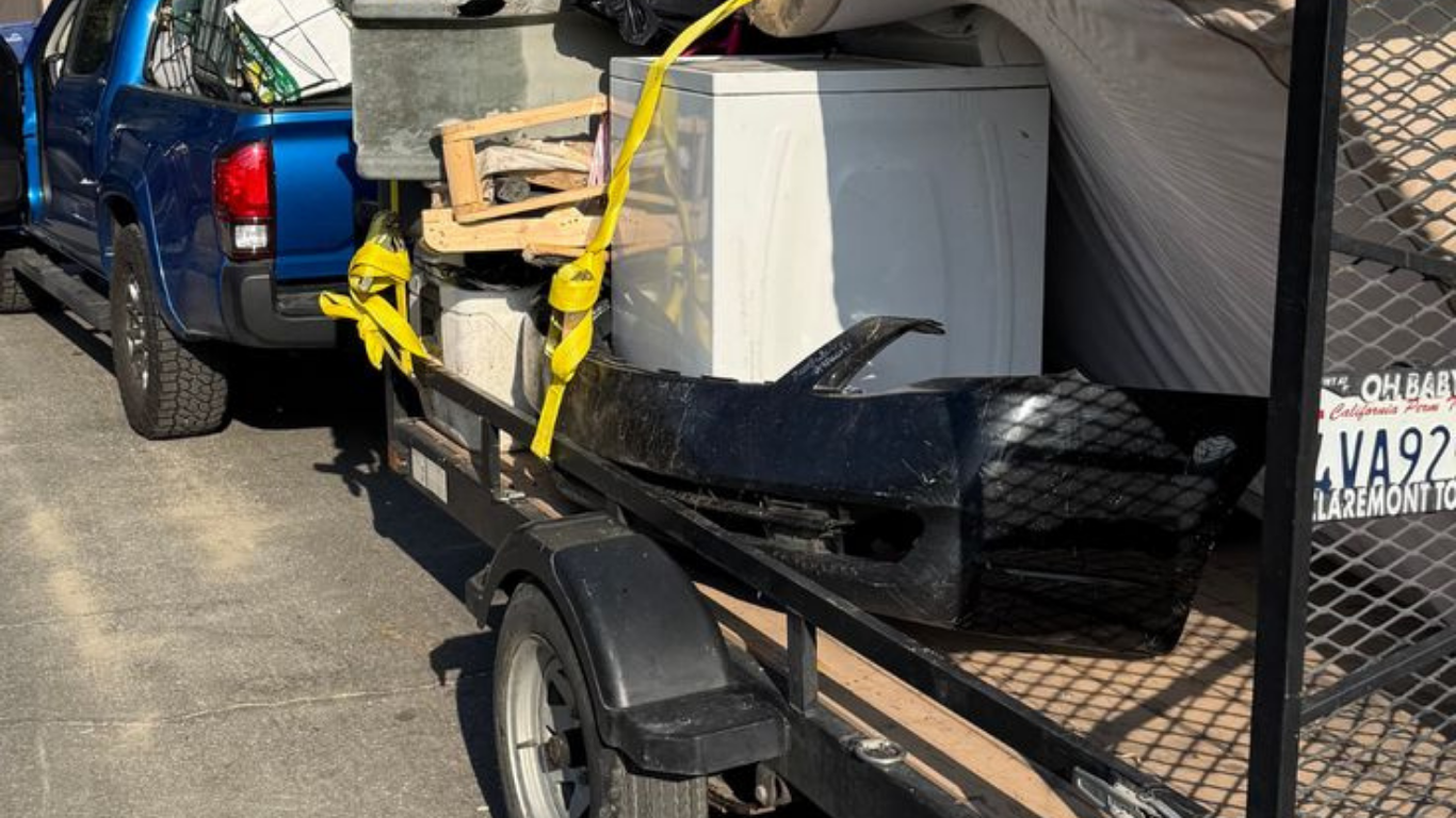 Truck pulling a trailer loaded with items, including a washing machine and bumper.