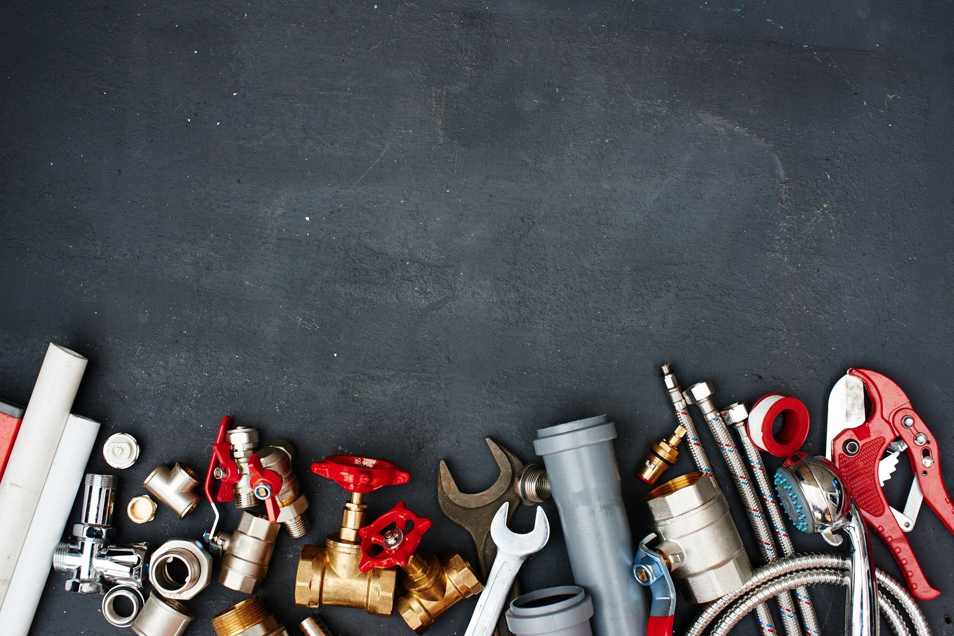 Assorted plumbing tools and pipe fittings arranged along the bottom of a dark surface. Assorted plumbing tools and pipe fittings arranged along the bottom of a dark surface.