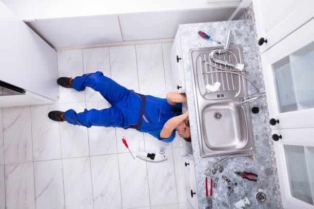 A male plumber from Advantage Plumbing, Inc. is lying on the floor providing plumbing services to a 
