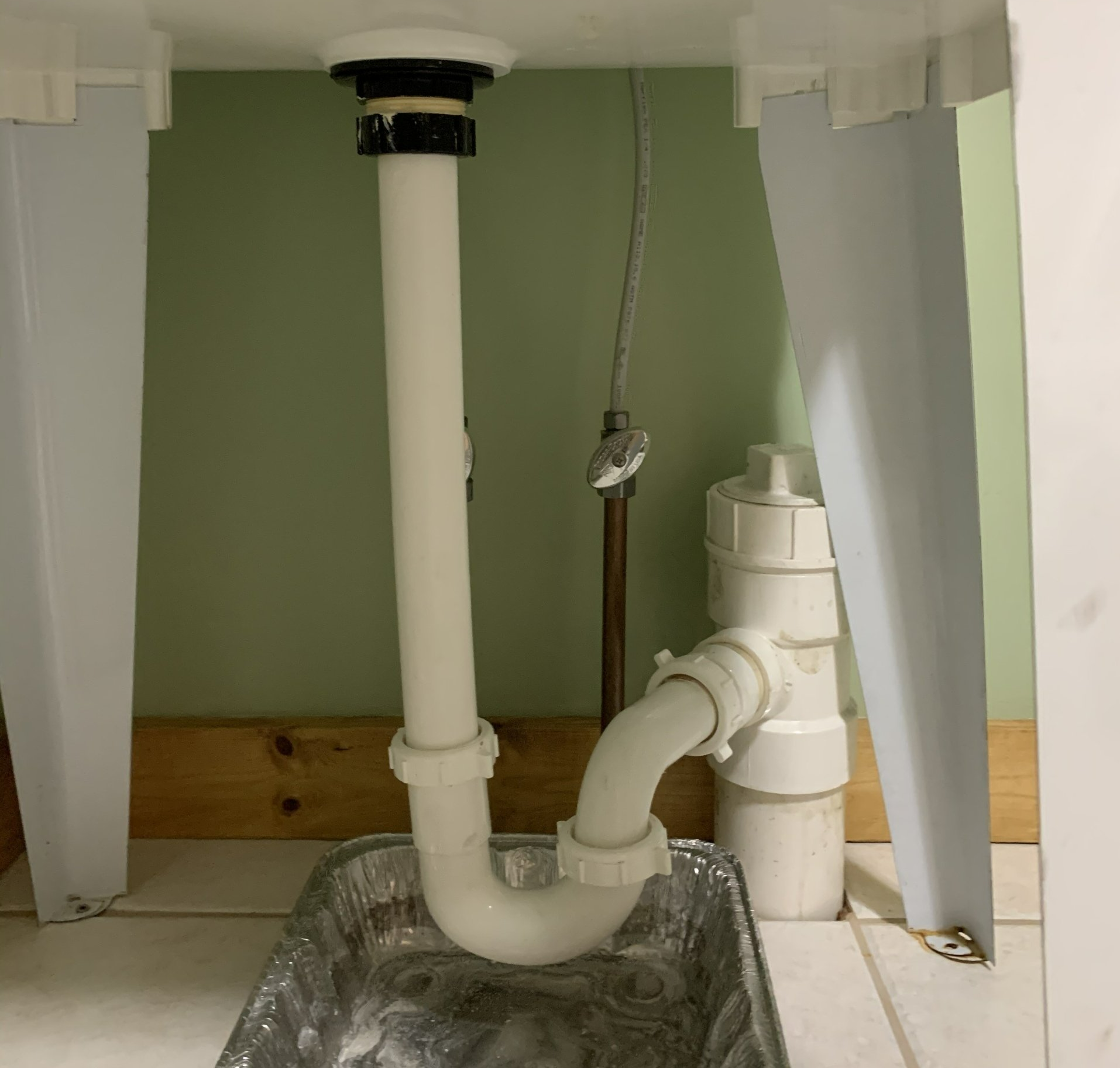 Under-sink plumbing: white pipes with a curved trap, connecting to drain and vent pipe, inside a cabinet.