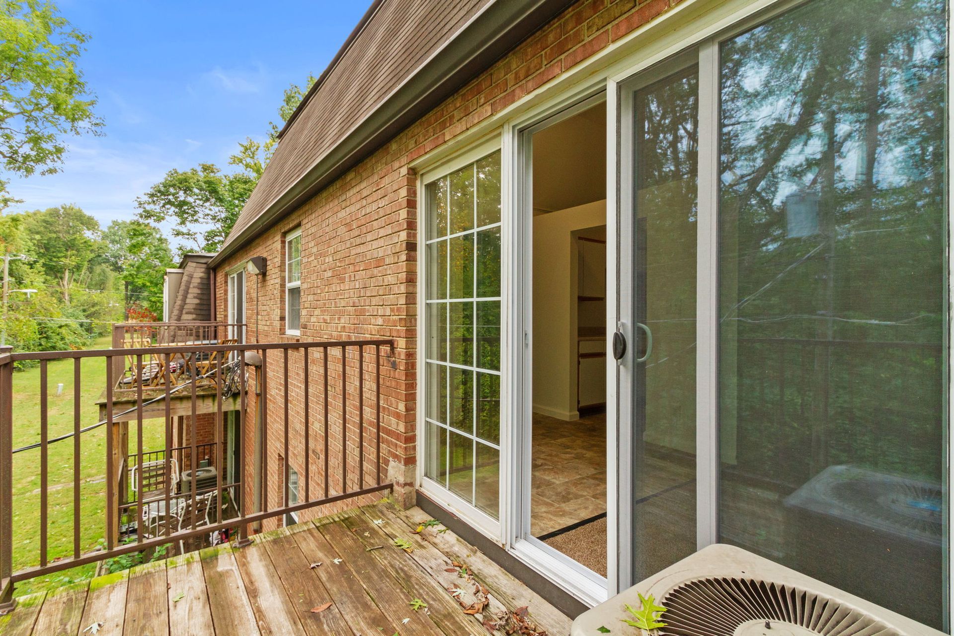 Exterior view of a balcony with sliding glass doors. Brick building with greenery visible.