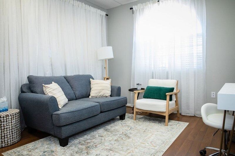 Bright living room with gray sofa, green accent chair, white curtains, floor lamp, and patterned rug.