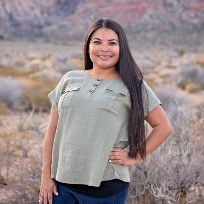 Smiling woman in an olive green top standing outdoors with mountains and dry brush behind her