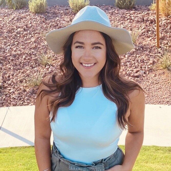 Smiling person in a light blue top and hat standing outdoors in sunlight