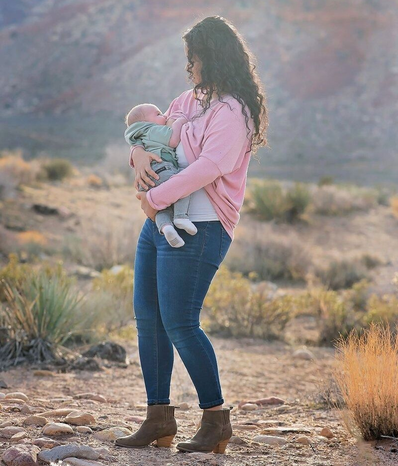 Woman in a pink sweater holding a baby outdoors in a rocky desert landscape.