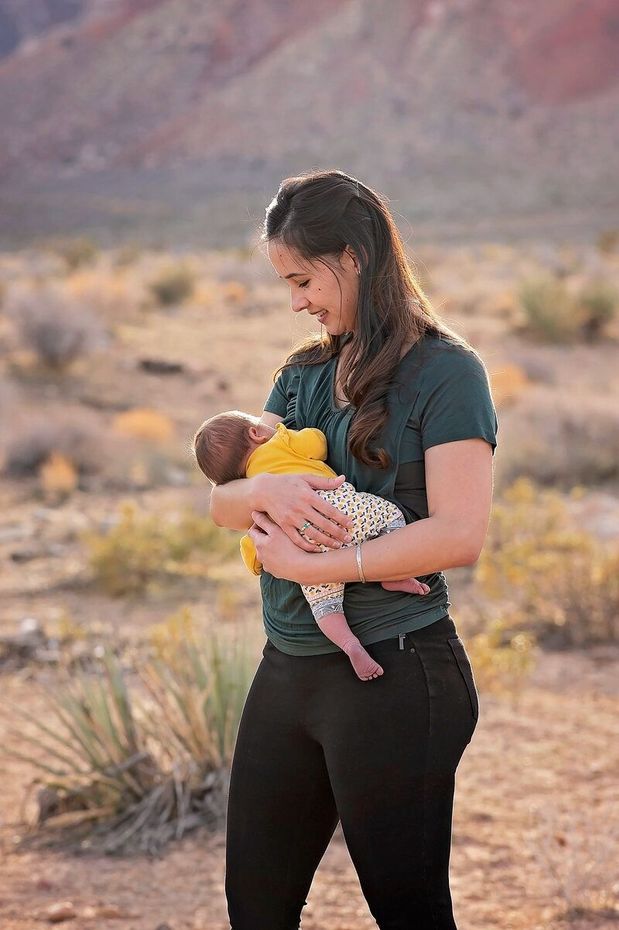 Woman holding a baby outdoors in a desert, with mountains and scrub in the background.