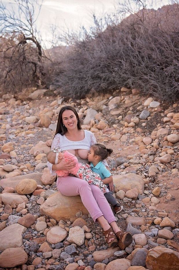 Woman sitting on rocky ground holding a child, with brush and trees in the background