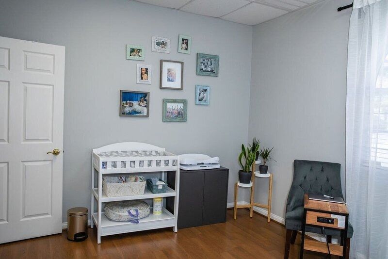 Bright nursery corner with crib, changing table, framed wall art, plant, and small chair by window