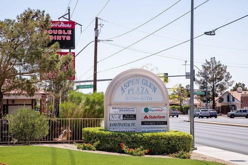 Entrance sign for Aspen Glen Plaza beside a street, with trees and storefronts in the background