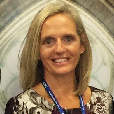 A woman with blonde hair and a lanyard around her neck is smiling for the camera.