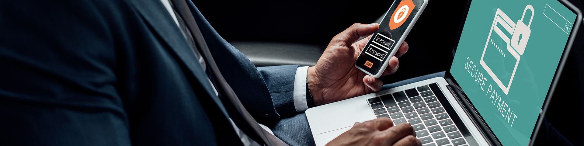 A man in a suit is holding a cell phone in front of a laptop.
