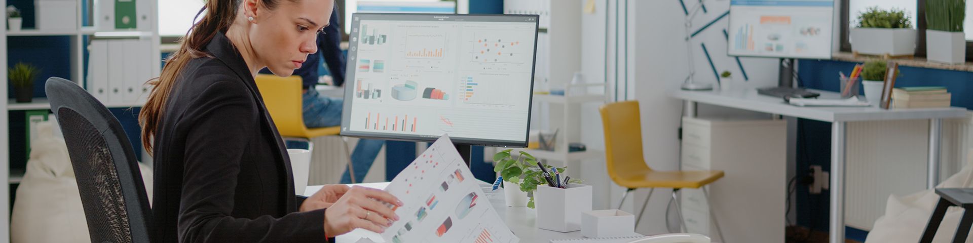 A woman is sitting at a desk in an office looking at papers.