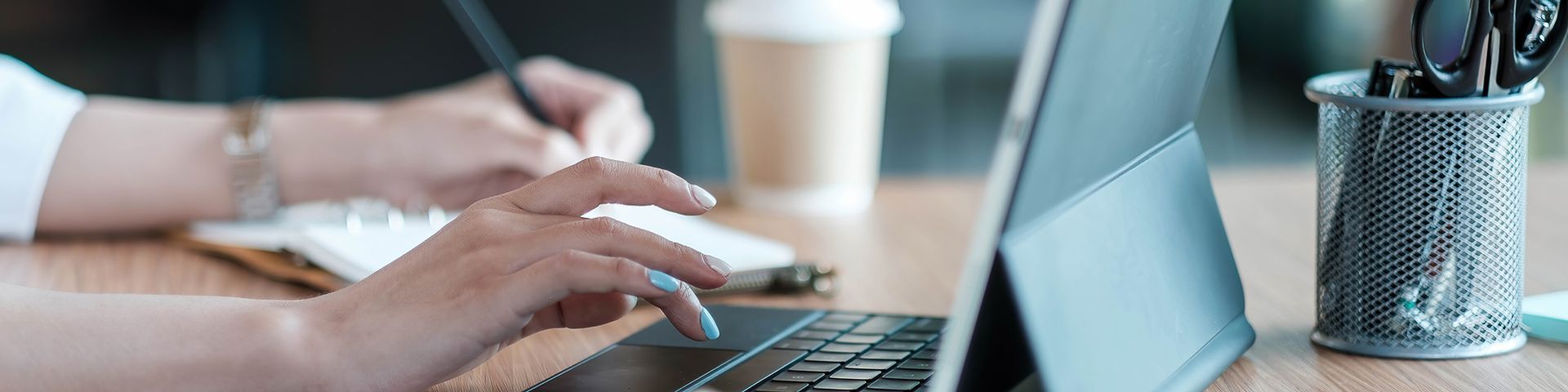 A person is typing on a laptop computer while holding a pen.