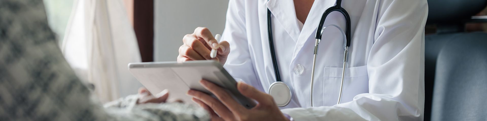 A doctor is talking to a patient while using a tablet computer.