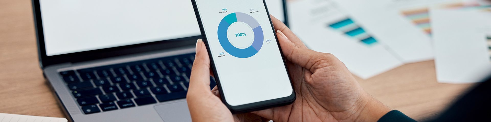 A person is holding a cell phone in front of a laptop.