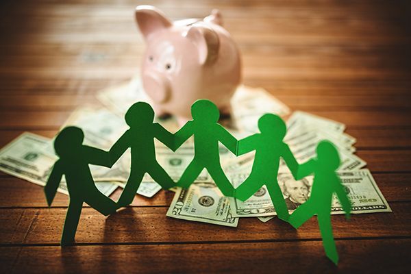 A group of paper people are holding hands in front of a piggy bank.