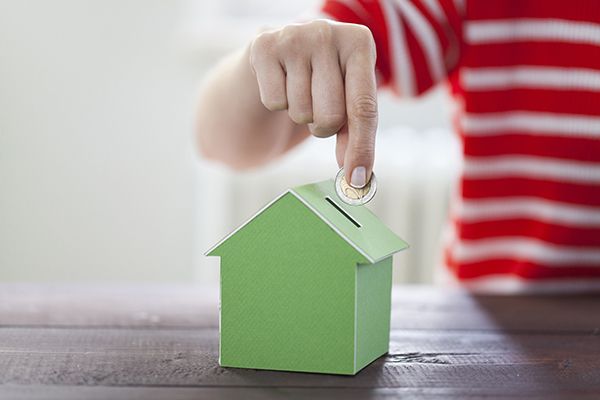 A person is putting a coin into a green house piggy bank.