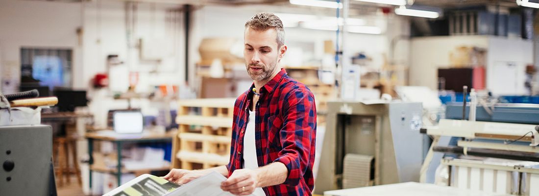 A man is standing in a factory holding a piece of paper.