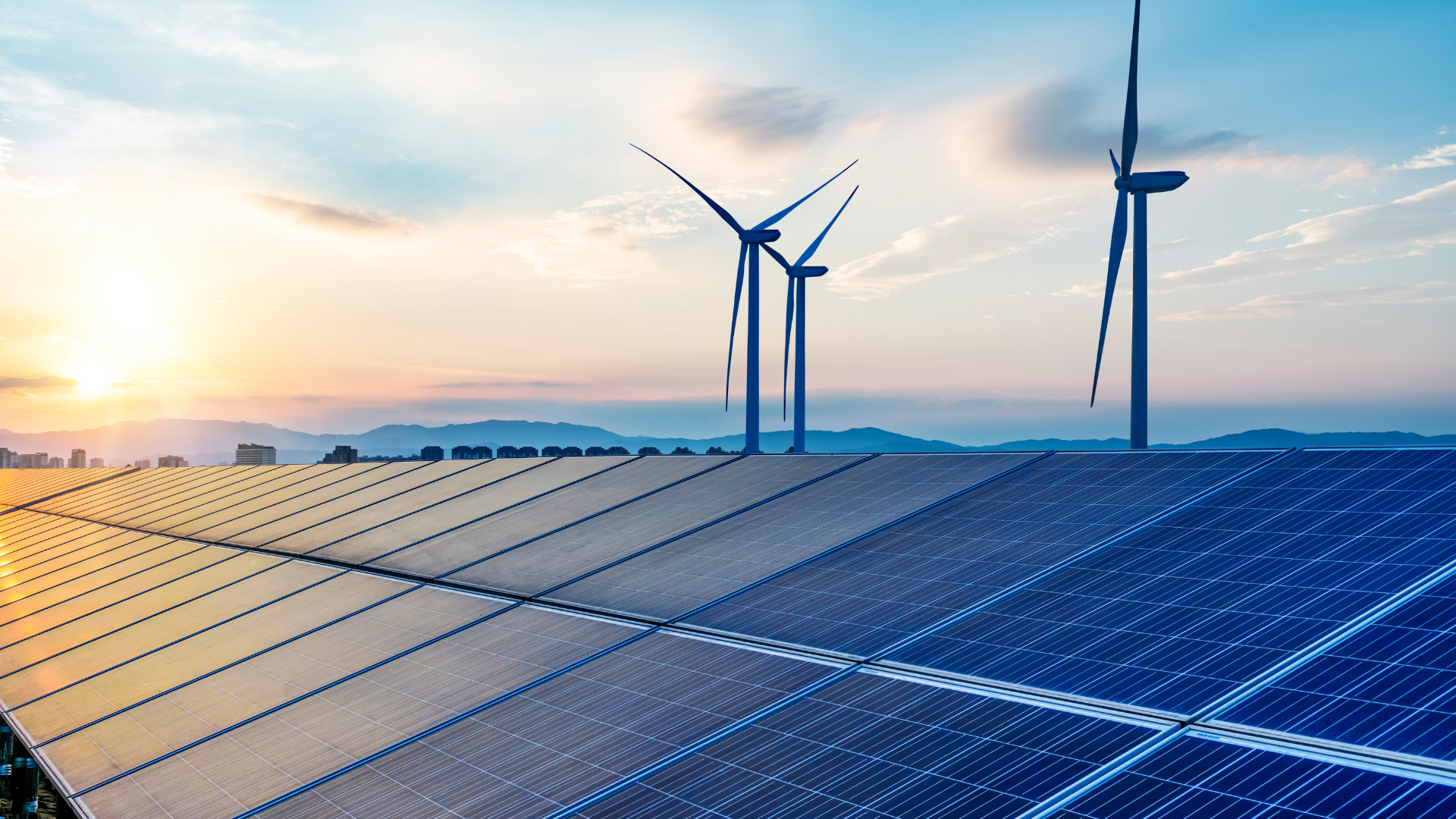 Solar panels in the foreground with wind turbines in the background under a sunrise sky.