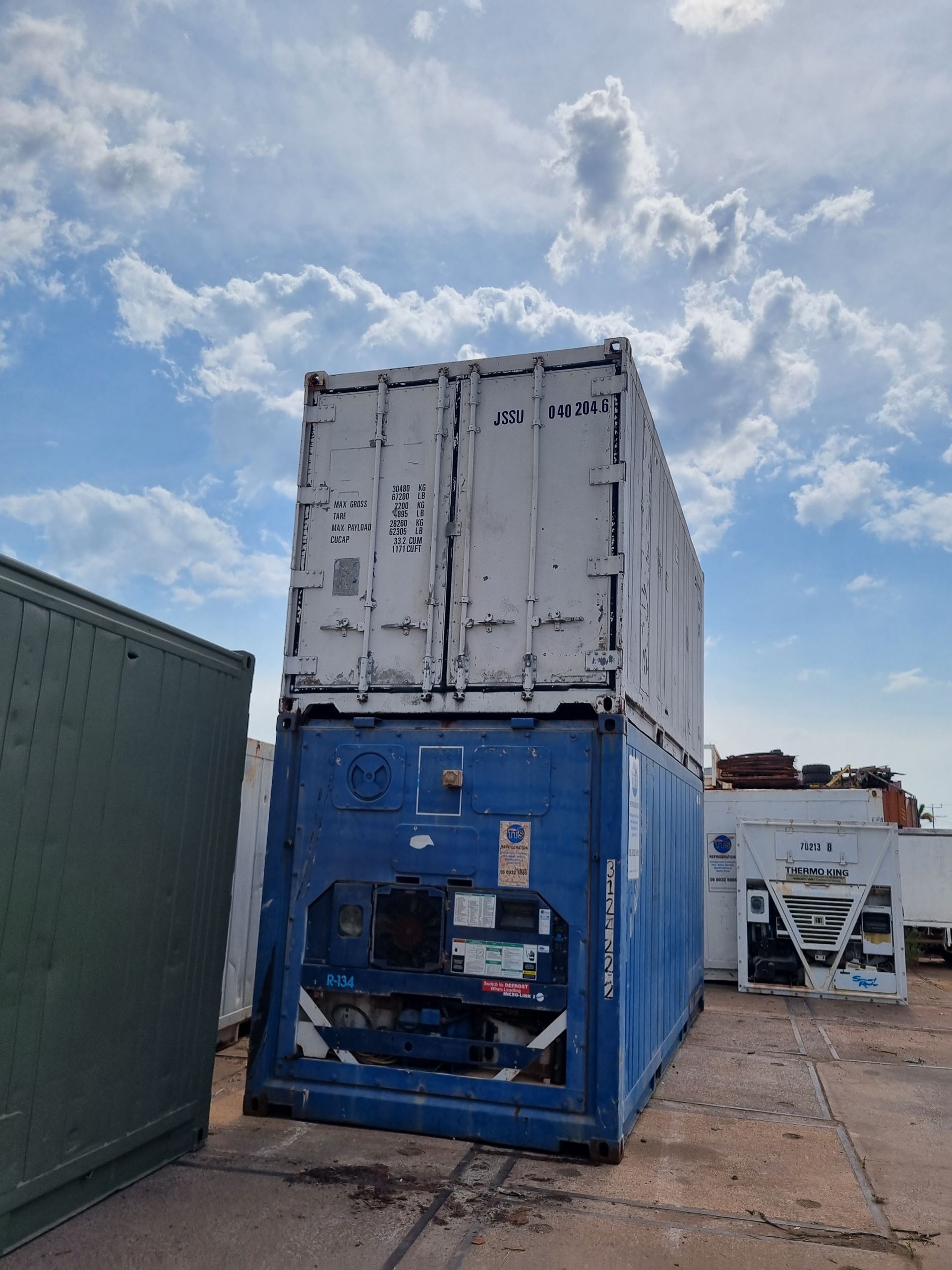 Two shipping containers stacked. Blue container on the bottom, white one on top, outdoors, cloudy sky — TTS Refrigeration in Pinelands, NT