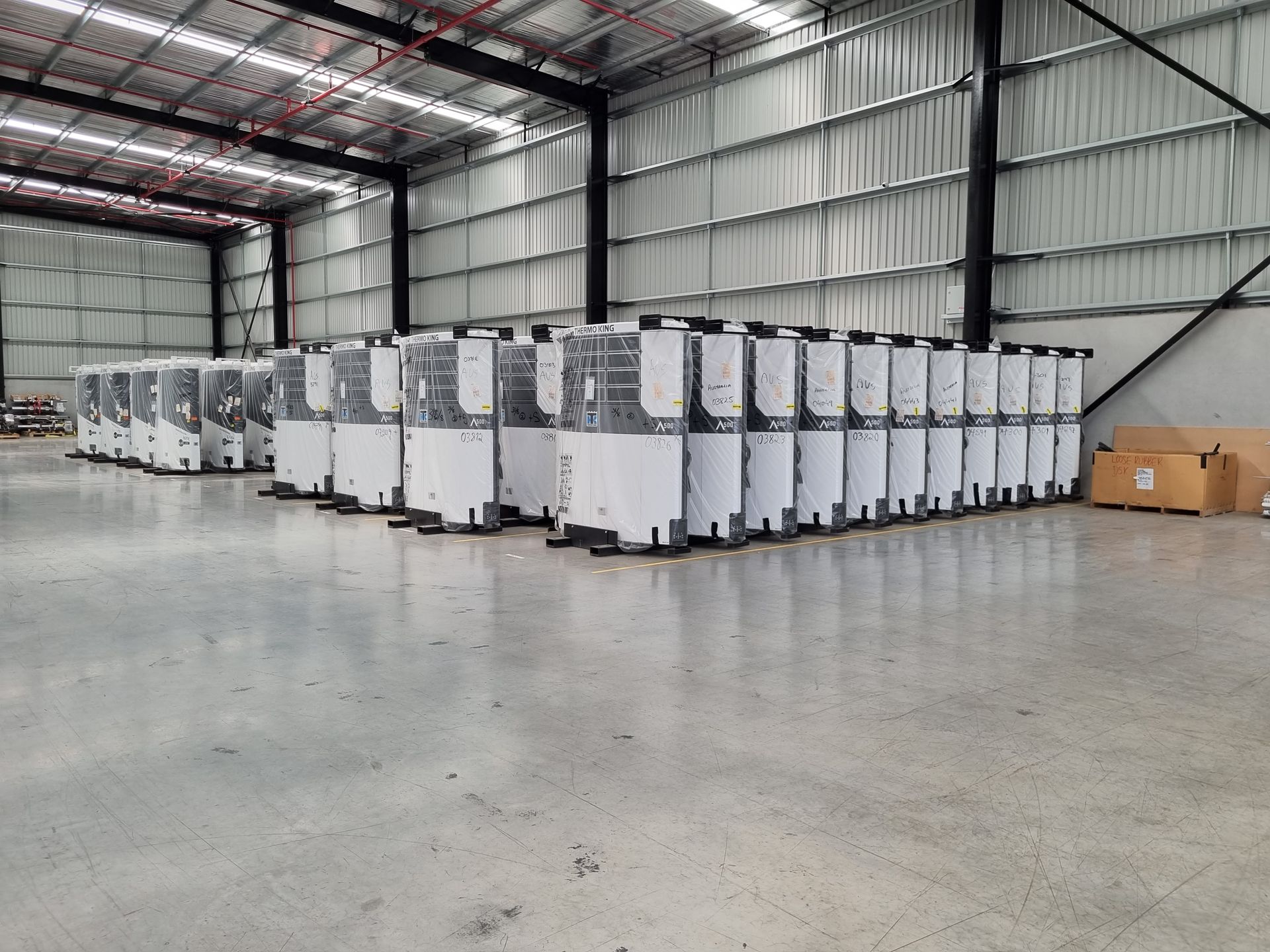 Rows of white industrial machines stored inside a large warehouse with a shiny gray floor — TTS Refrigeration in Pinelands, NT