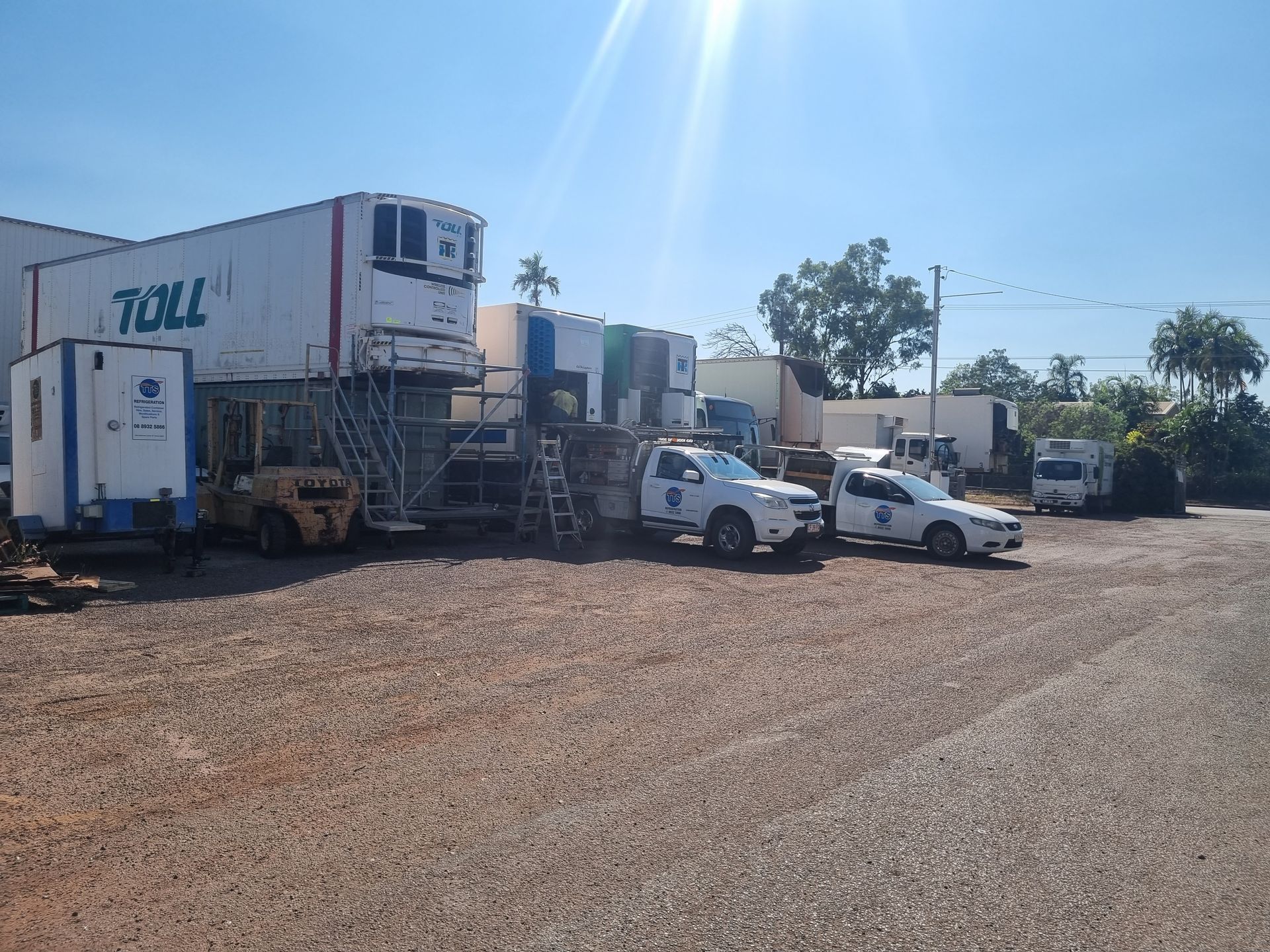 White Toll container and vehicles parked on gravel under a sunny sky — TTS Refrigeration in Pinelands, NT