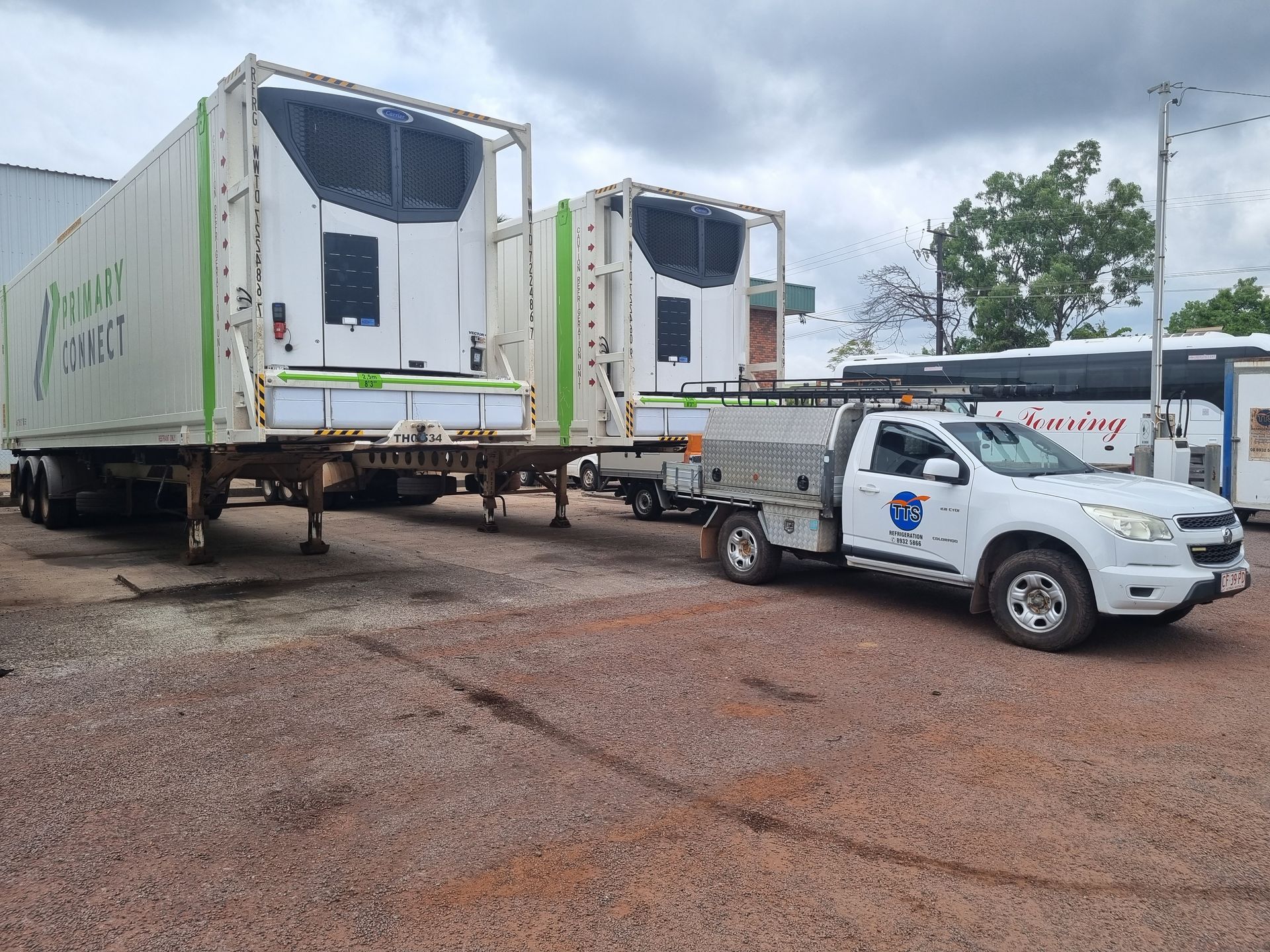 White refrigerated trailers with green trim, parked near a white service truck on gravel. Cloudy sky — TTS Refrigeration in Pinelands, NT