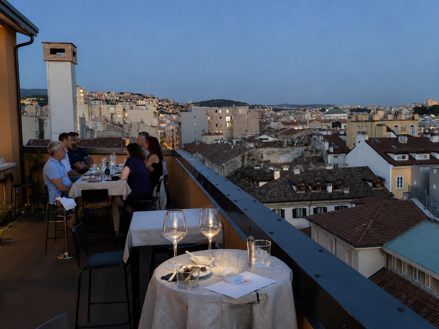 Ristorante panoramico sul tetto al tramonto, con commensali e tavoli illuminati a lume di candela