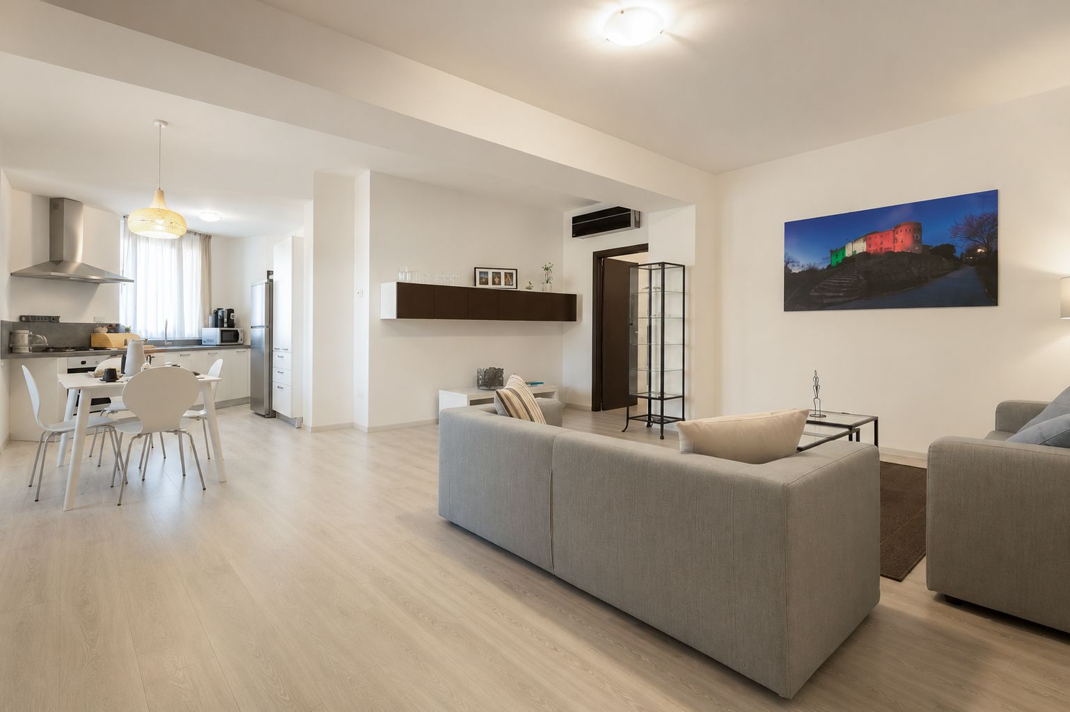 Luminoso soggiorno open space con divani grigi, tavolo da pranzo, cucina e opere d'arte alle pareti
