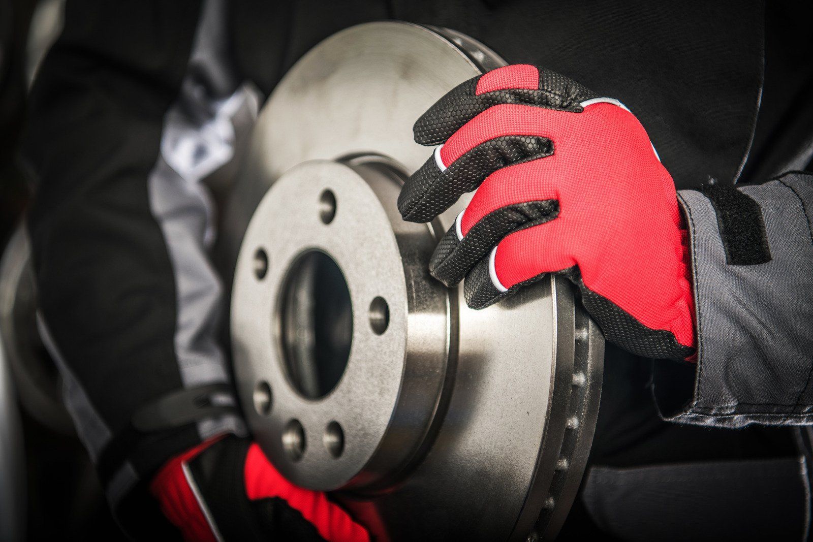 A person wearing red gloves is holding a brake disc.
