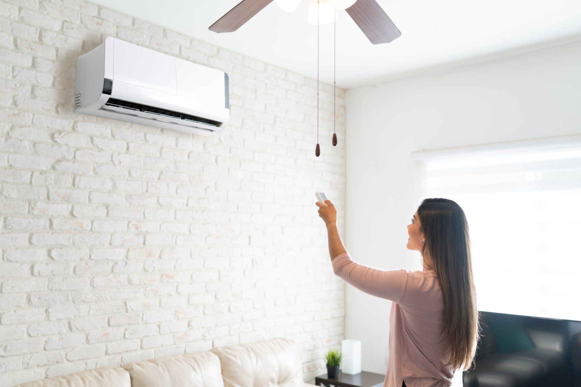 A woman is adjusting the air conditioner in her living room with a remote control.