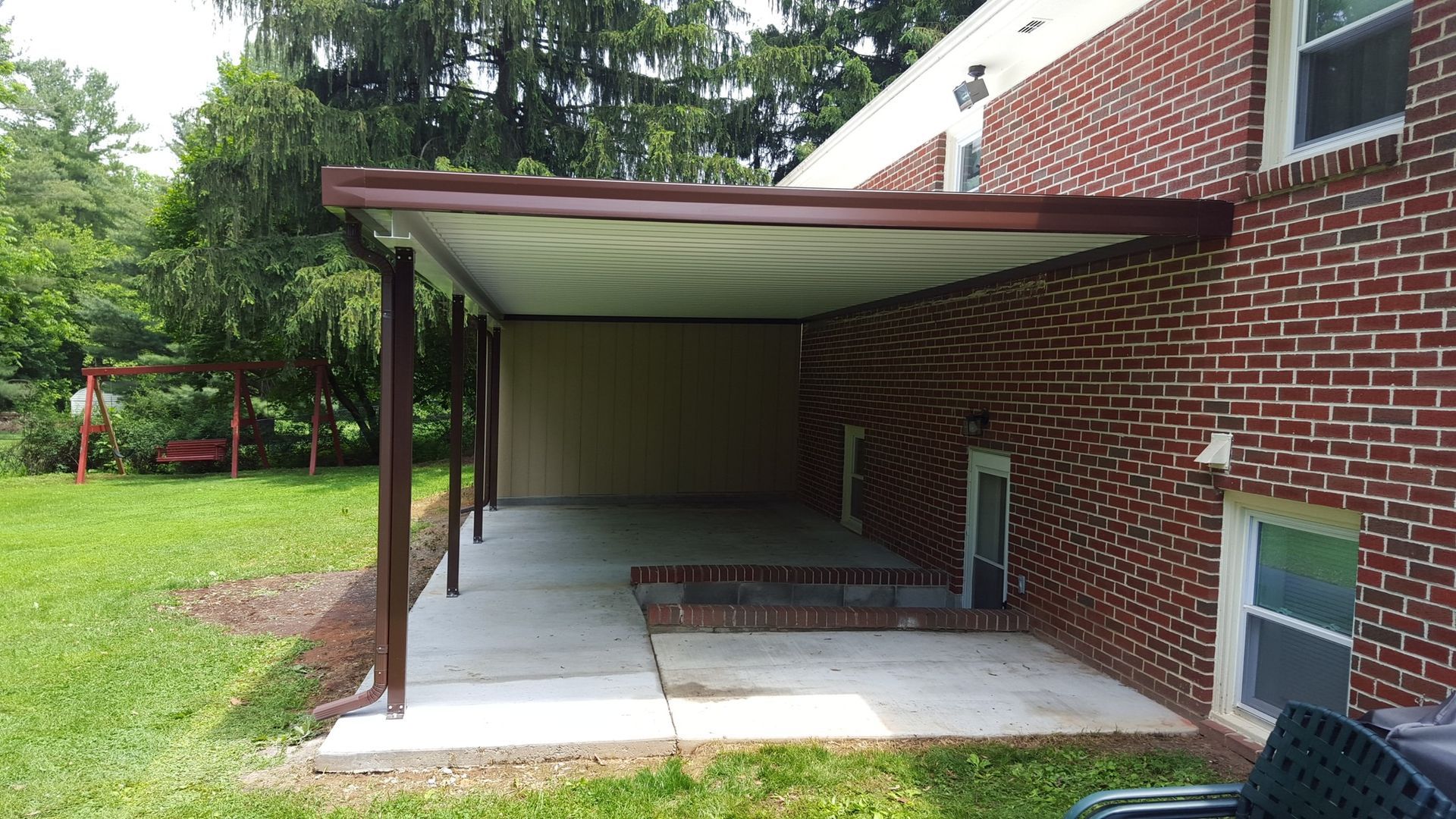 There is a carport in the backyard of a brick house.