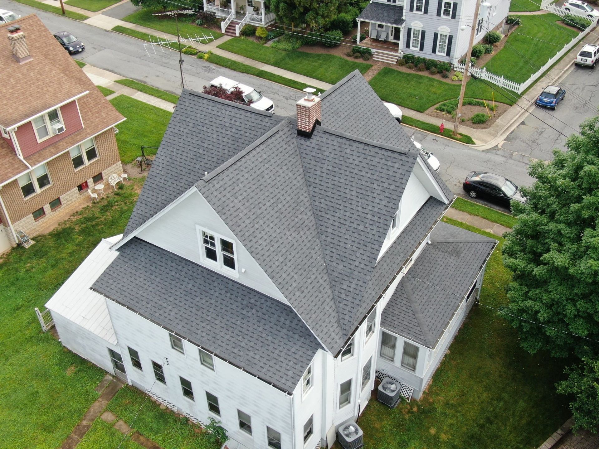 An aerial view of a white house with a gray roof in a residential neighborhood.