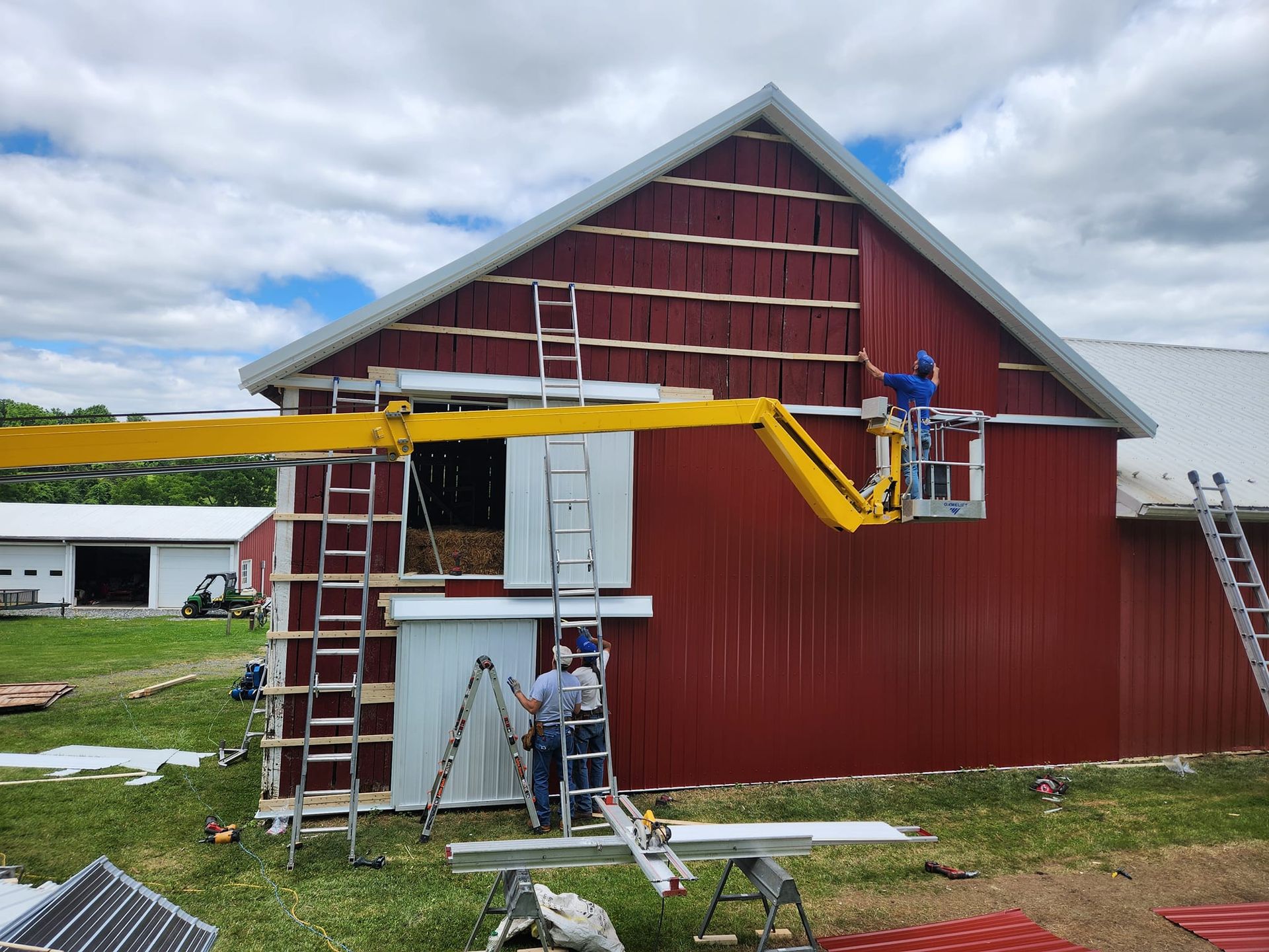 Two men are working on a red barn with a crane attached to it.