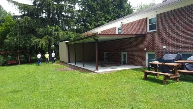 A group of people standing in front of a brick building with a picnic table and grill.