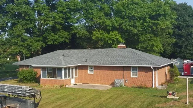 A brick house with a gray roof is sitting on top of a lush green lawn.