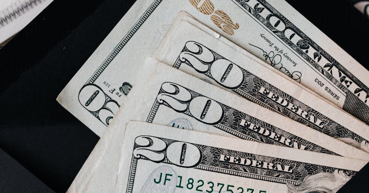 Several twenty-dollar bills fanned out on a black surface. The bills are white, green, and have black detailing.