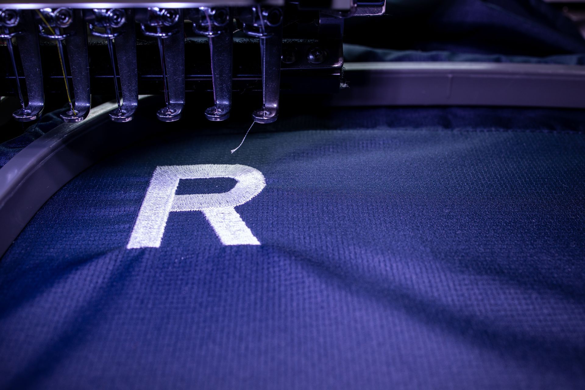 An industrial embroidery machine stitching a white letter 